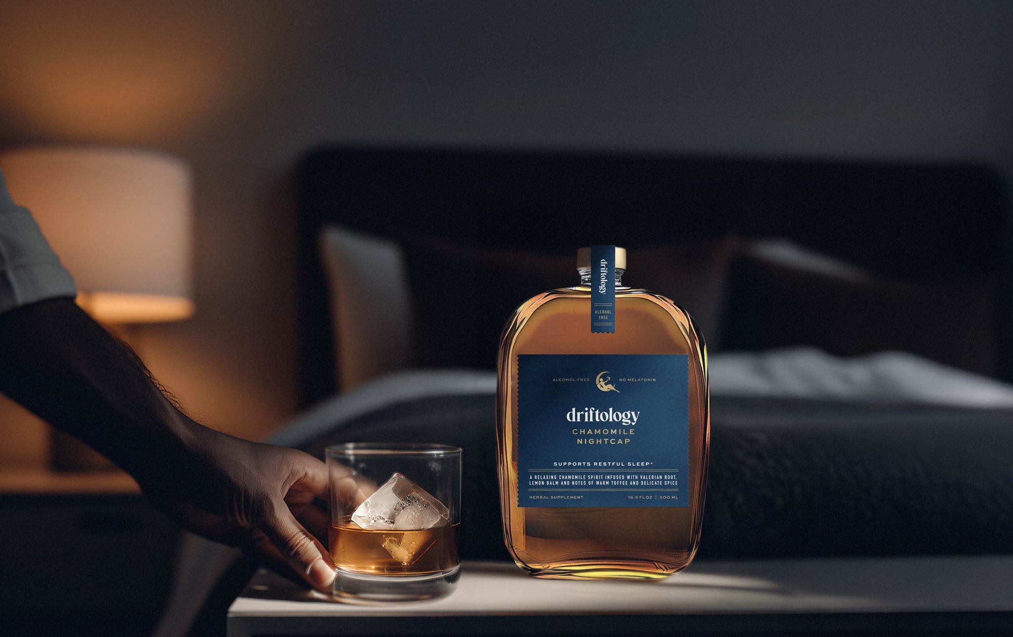 Bottle of Driftology Non-alcoholic Chamomile Nightcap with a glass on a table in a bedroom